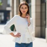 Młoda kobieta w białej bluzce peplum i jeansach na tle miejskiej ulicy w naturalnym świetle
